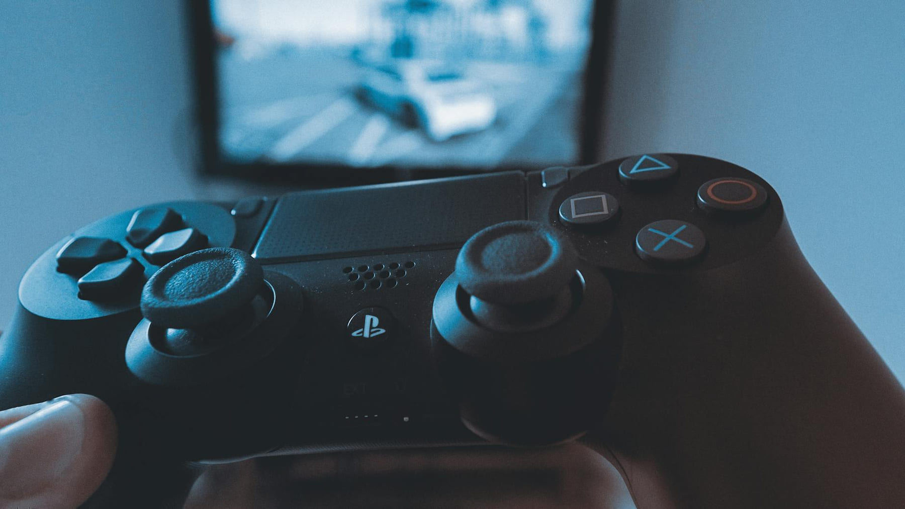 A hand holding a wireless game controller in front of a blurry screen, capturing the gaming experience. on The Loading Screen