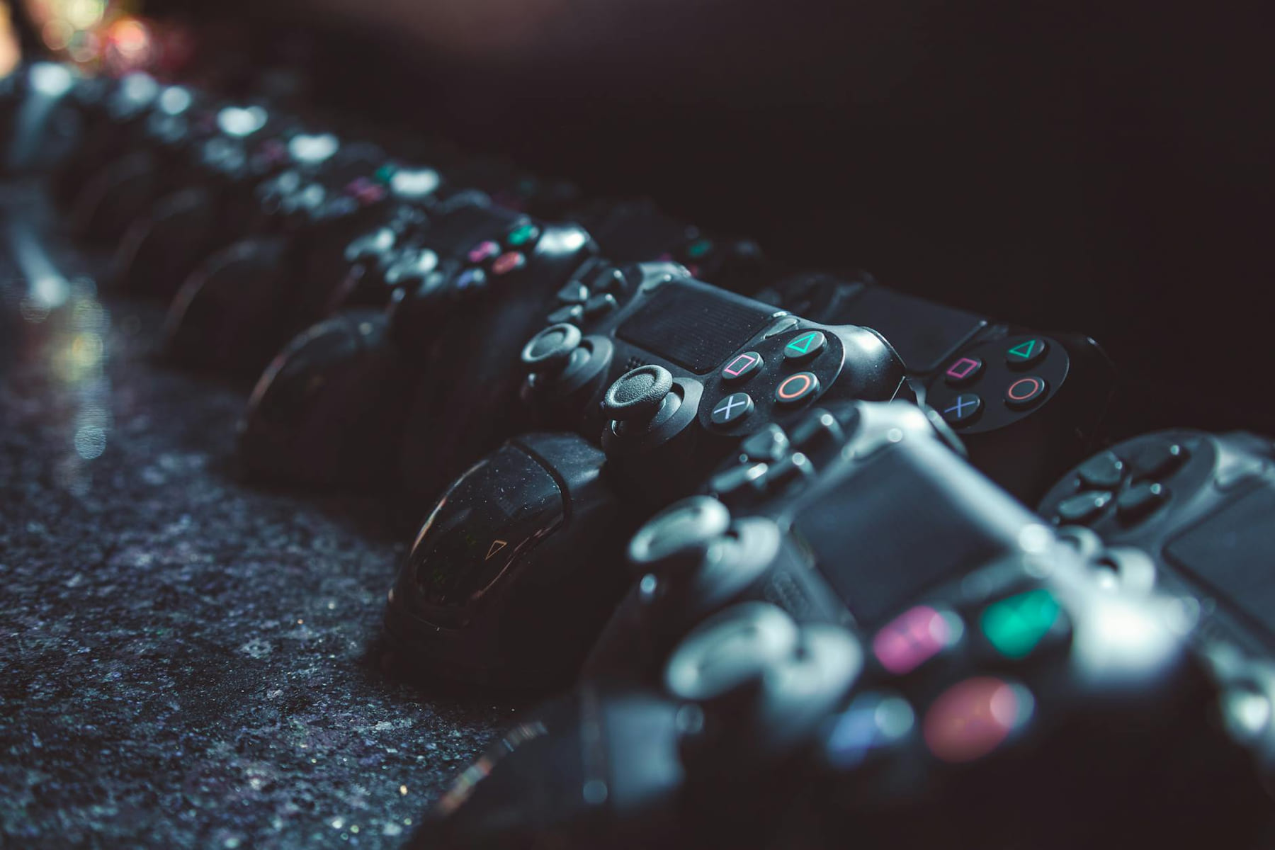 Series of gaming controllers lined up on a reflective surface, dimly lit. on The Loading Screen