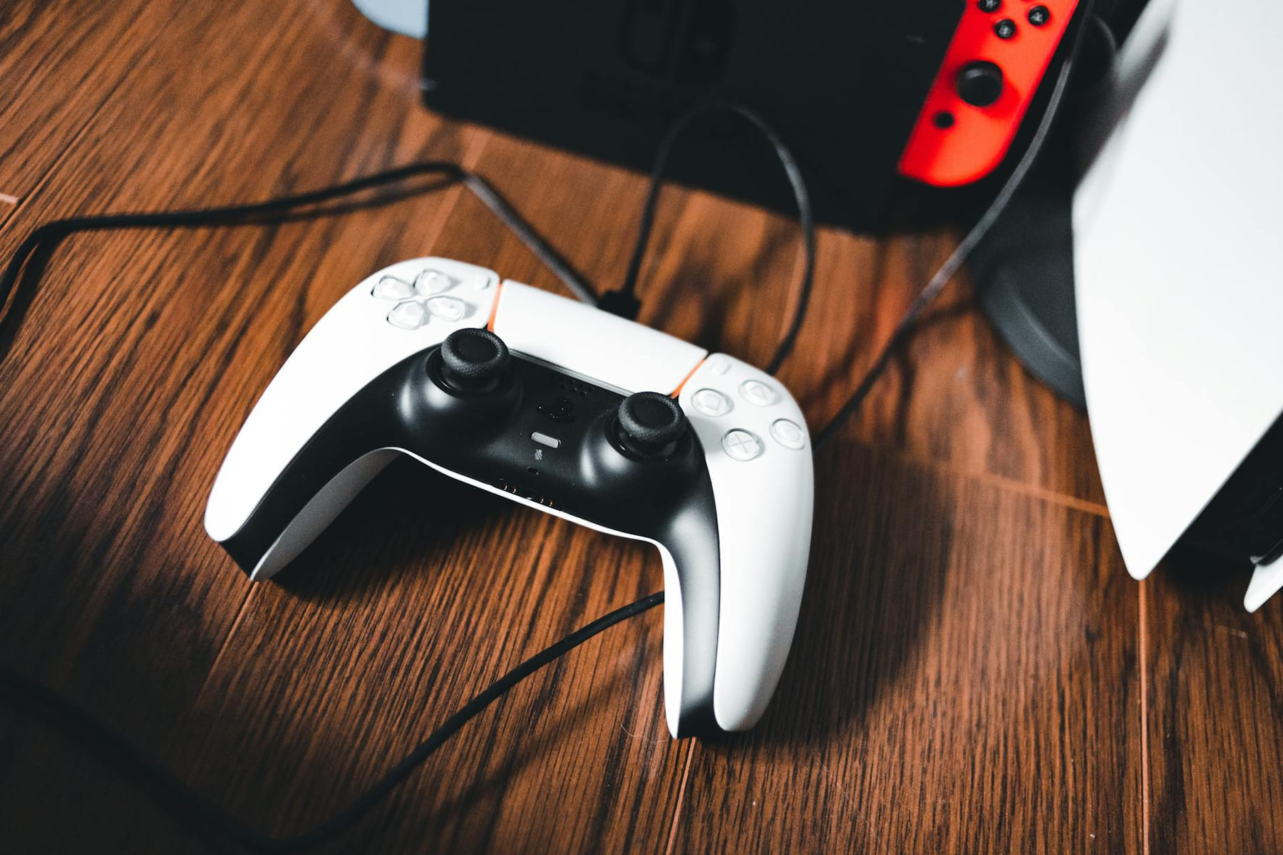 A gaming controller laying on a wooden table next to other gaming devices. on The Loading Screen