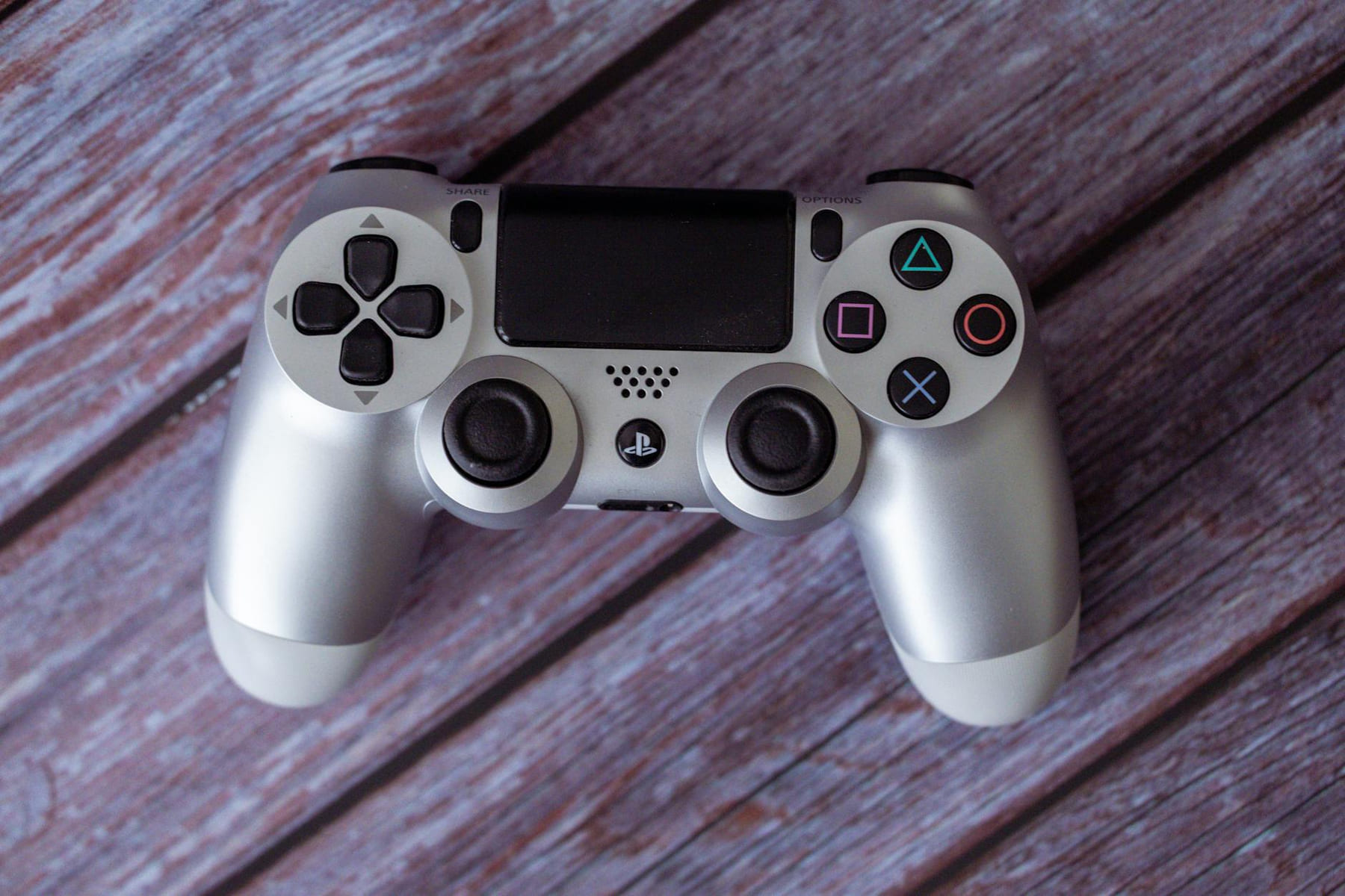 Top view of a silver PlayStation controller on a rustic wooden background. on The Loading Screen
