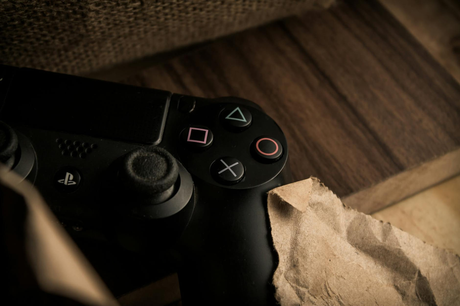A close-up of a PlayStation gaming controller resting on a wooden surface with a rustic feel. on The Loading Screen