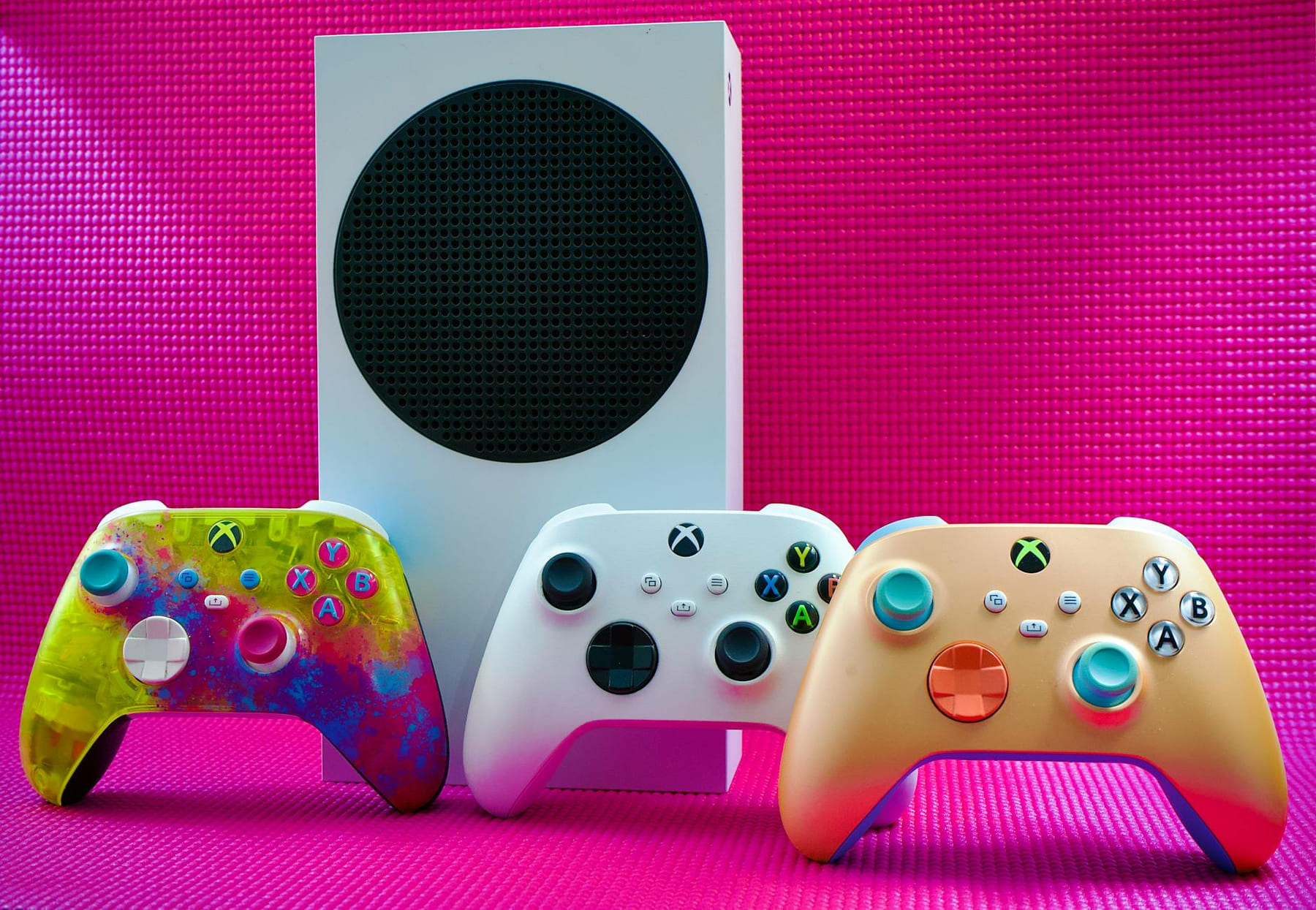 Vibrant gaming controllers displayed with a console on a bold pink backdrop. on The Loading Screen